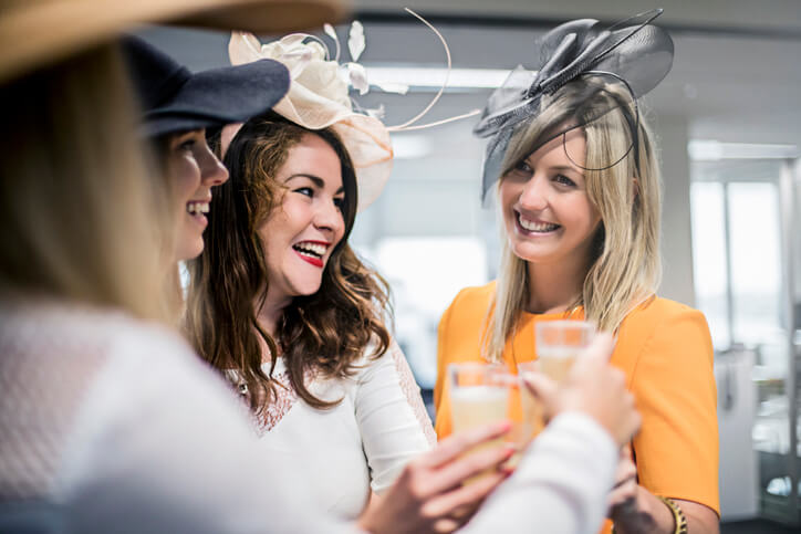 Ladies celebrating Kentucky Derby with fancy hat and a drink in their hand.